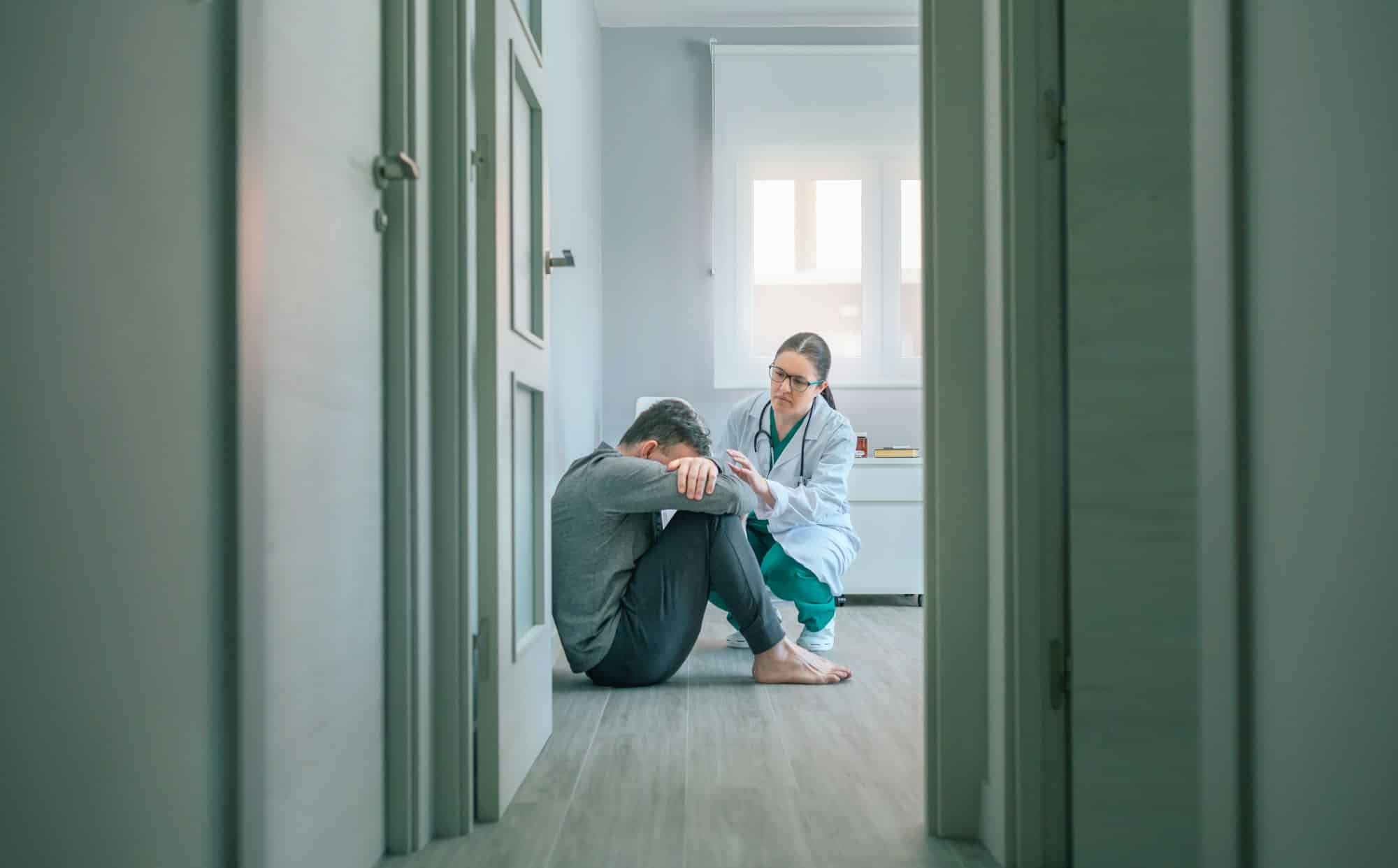 Psychiatrist talking to patient with mental disorder and suicidal thoughts sitting on room floor